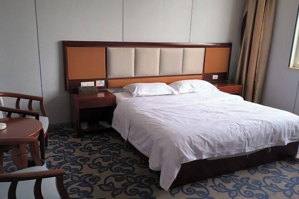 A hotel room with a bed, wooden nightstands, a chair, and a patterned carpet.