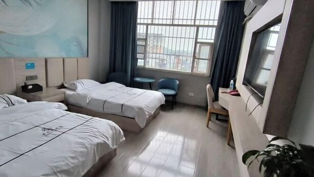 A hotel room with two beds, a desk, a chair, a TV, and a large window with curtains. - Zhengyue Hotel (Qianjiang)