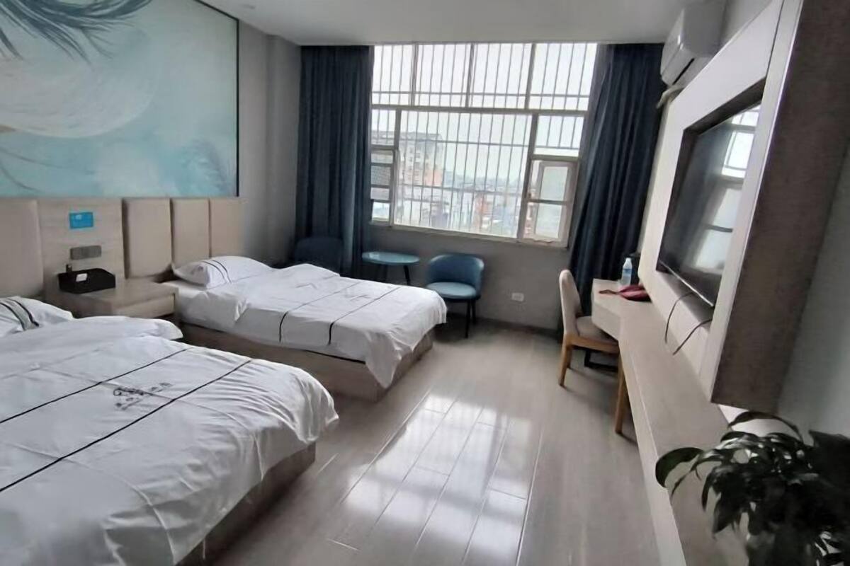 A hotel room with two beds, a desk, a chair, a TV, and a large window with curtains.