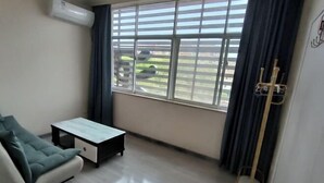 A room with a sofa, a small table, a window with blinds, and a coat rack. - Zhengyue Hotel (Qianjiang)