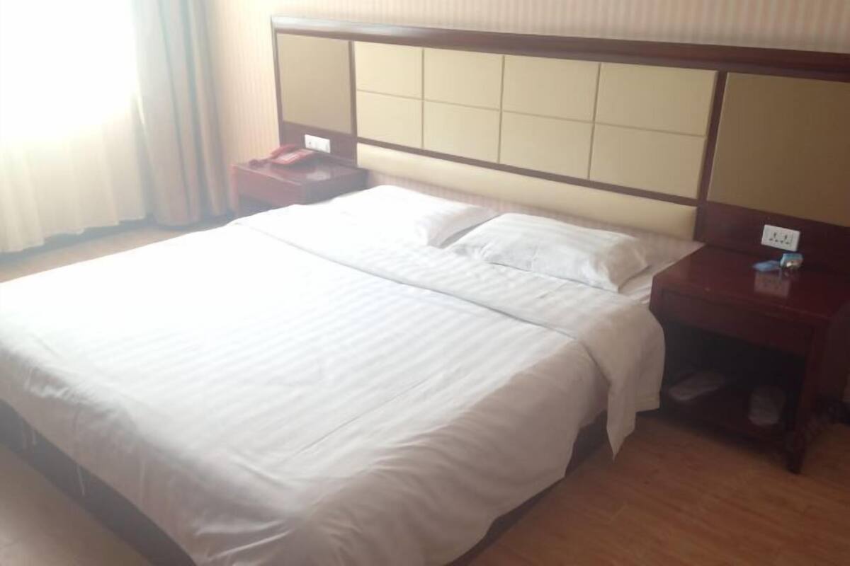 A hotel room with a large bed, wooden headboard, and a nightstand with a phone and a small table.