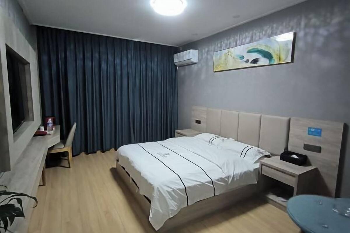 A hotel room with a bed, bedside table, chair, and a desk with a computer.