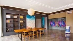 A modern dining area with a wooden table and chairs, a large bookshelf, and a colorful abstract painting on the wall.