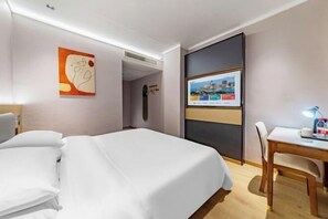 A hotel room with a bed, a desk with a chair, a TV, and a painting on the wall. - Xinghao Zunxu Hotel (Rui'an)