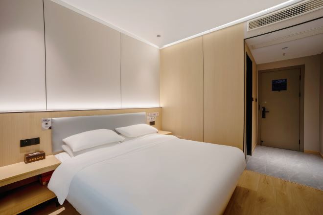 A hotel room with a bed, bedside table, and a door leading to another room.