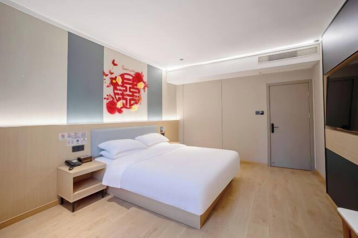 A modern hotel room with a bed, bedside table, and a wall-mounted artwork.