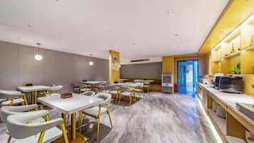 Un espace de restauration moderne dans un hôtel, avec plusieurs tables et chaises, un coin cuisine et une vue sur la rue.