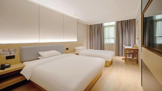 A hotel room with two beds, a desk, and a TV.