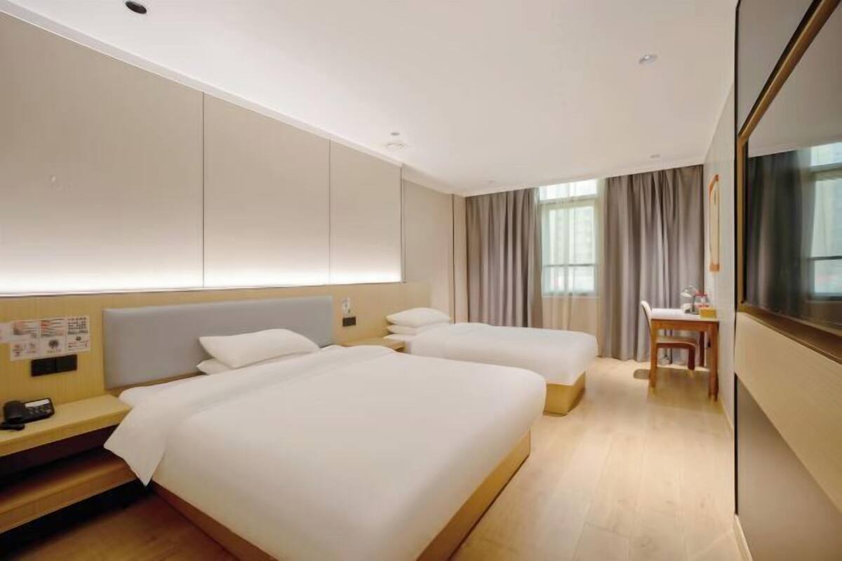 A hotel room with two beds, a desk, and a TV.