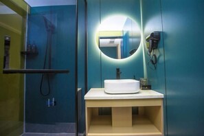 Un baño con cabina de ducha de vidrio, un espejo redondo y un lavabo con toallero.