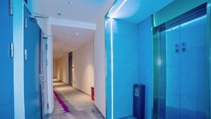 A modern hallway with a blue-lit elevator, a trash bin, and a patterned carpet.