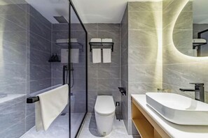 Un baño moderno con ducha de vidrio, inodoro blanco y tocador curvo con un espejo grande.