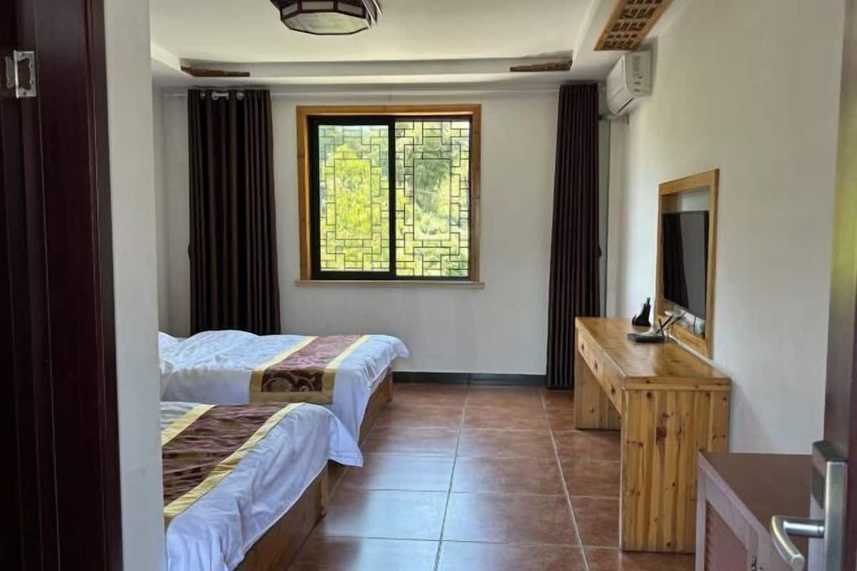 Una habitación con dos camas, un escritorio de madera, un espejo y una ventana con vistas.