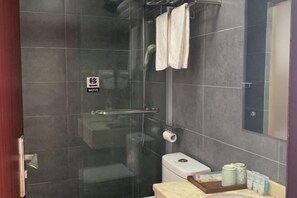 Un baño moderno con cabina de ducha de vidrio, inodoro y zona de lavamanos con artículos de aseo.