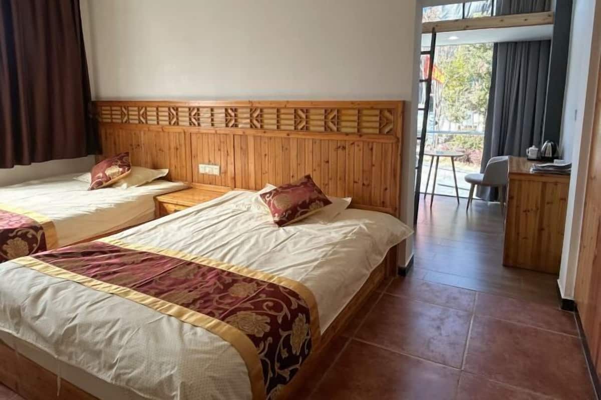 Habitación de hotel con dos camas, cabecero de madera, una mesita y vista al exterior.