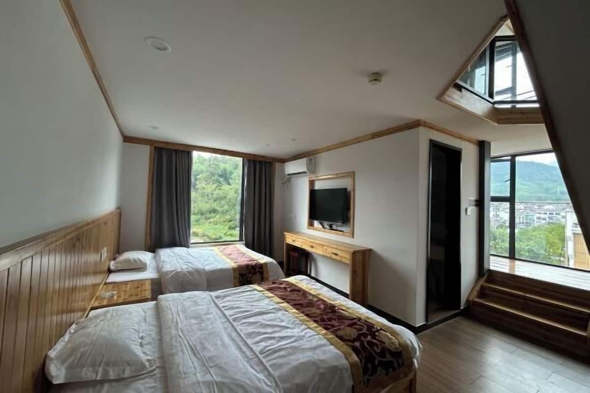 Un dormitorio con dos camas, televisor, escritorio y un amplio ventanal con vistas.