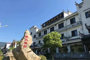 A traditional building with a sign in Chinese characters, a stone with inscriptions, and a clear blue sky.