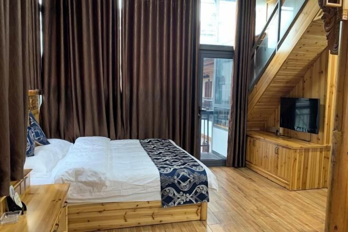 Una habitación de madera con cama, cortinas, televisor y balcón.