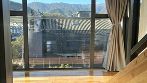 A room with large windows, wooden flooring, and a view of mountains and buildings. - Hongcun Huifeng Yayun Hotel (Yi County)