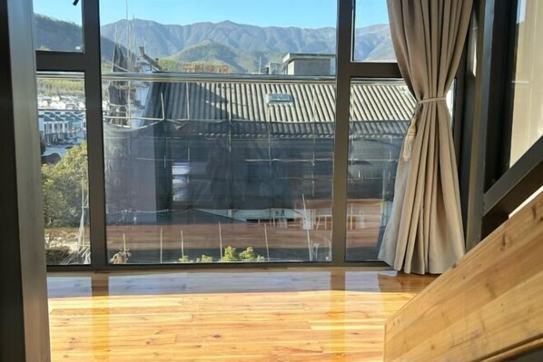 Una habitación con ventanas amplias, suelo de madera y vistas a montañas y edificios.