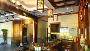 A reception area with a wooden counter, a computer, and a desk with a chair. - Hongcun Huifeng Yayun Hotel (Yi County)