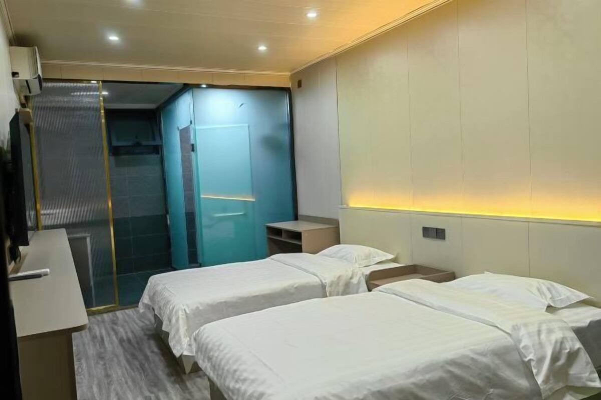 A hotel room with two beds, a desk, a shower area, and a wardrobe.