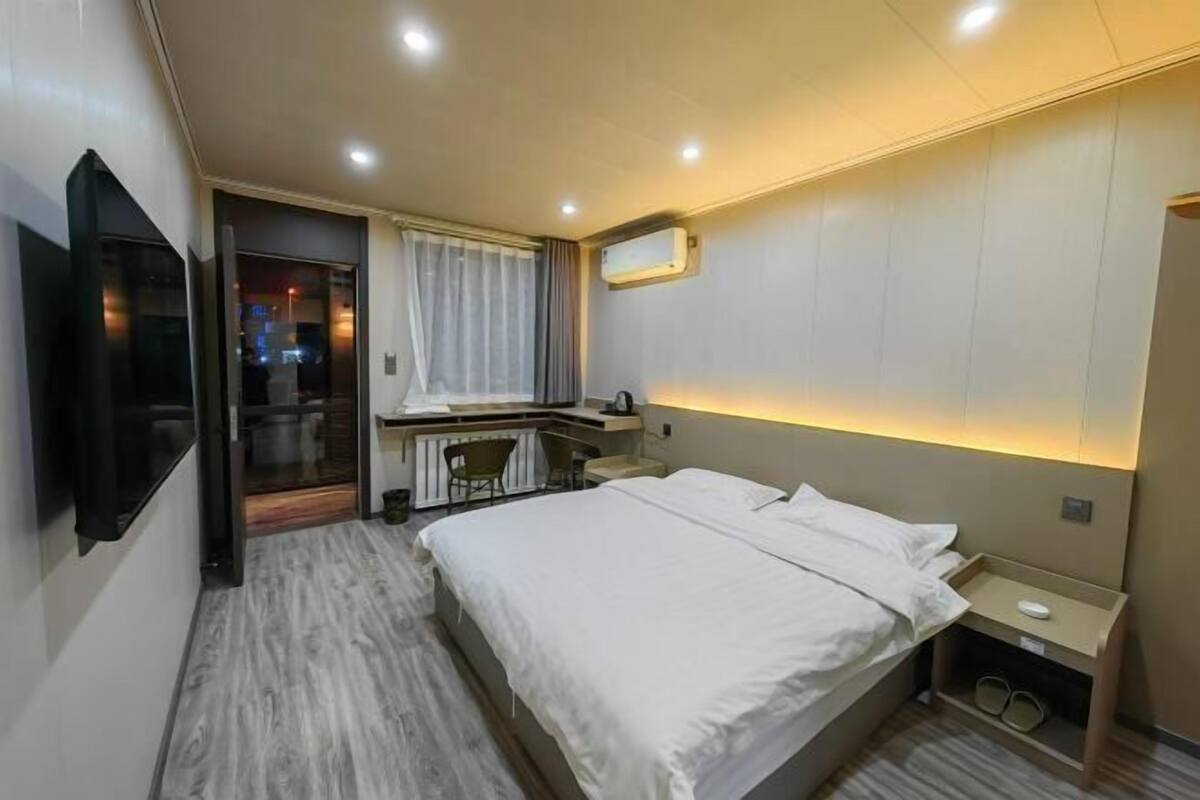 A hotel room with a bed, a desk, a chair, a TV, and a window with curtains.