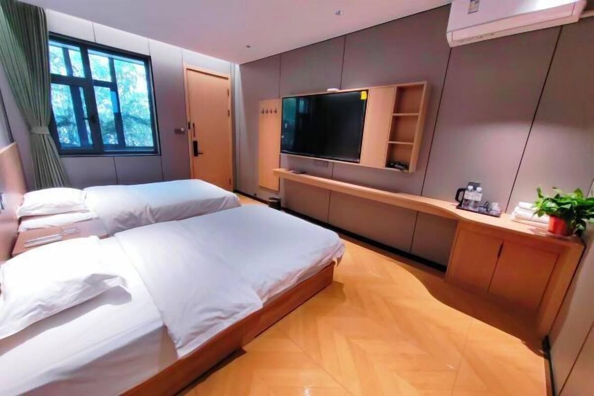 A hotel room with two beds, a TV, a plant, and a window with curtains.