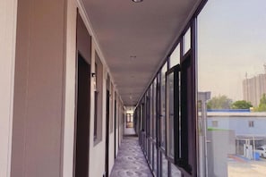 Un couloir avec des portes d’un côté et des fenêtres de l’autre, qui mène à un parking.