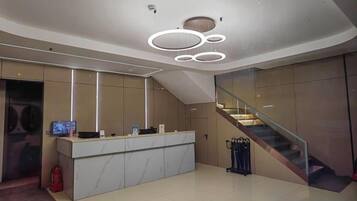 A modern reception area with a marble counter, a digital screen, and a staircase.
