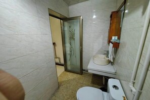 Un baño con inodoro, lavamanos y una puerta de cristal que da a otra habitación.