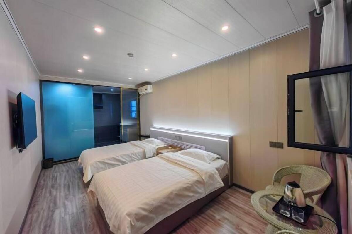 A hotel room with two beds, a large mirror, a wicker chair, and a small table with glasses.