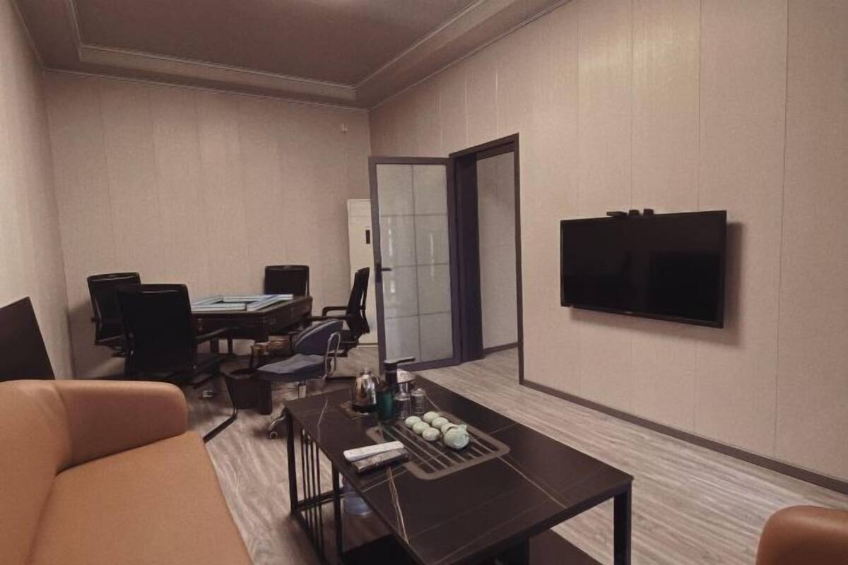 A hotel room with a television, a desk with chairs, a sofa, and a door leading to a bathroom.