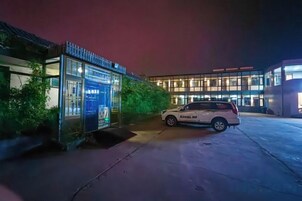 Un edificio con fachada de vidrio, un coche estacionado y una pequeña estructura con un letrero azul.