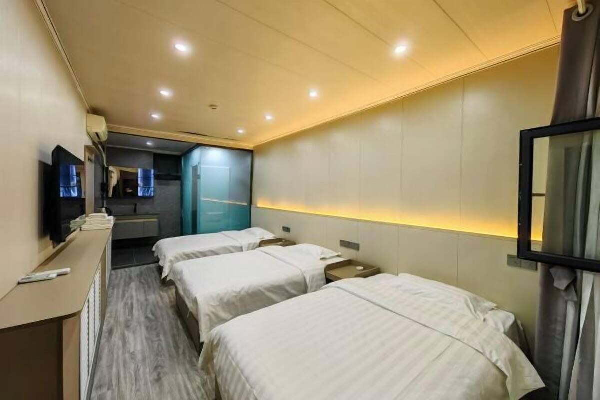 A hotel room with three single beds, a desk with a chair, a flat-screen TV, and a mirror on the wall.
