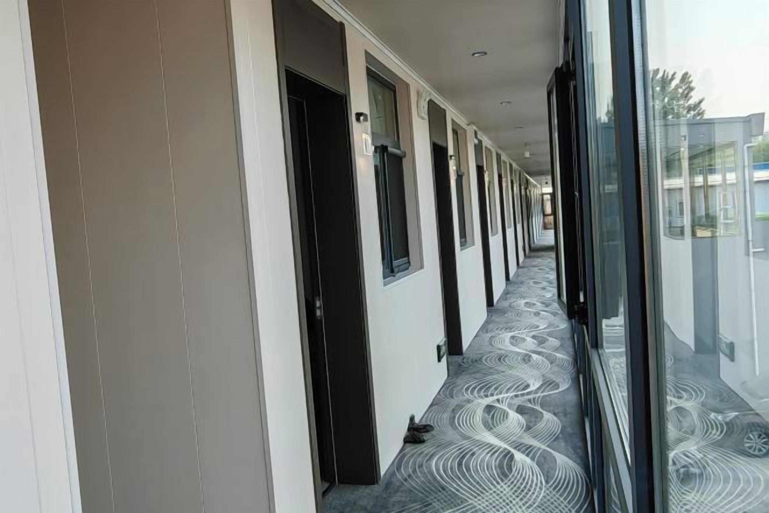 A corridor with doors leading to rooms, a patterned carpet, and a glass wall reflecting the outside.