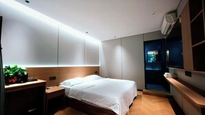 Quarto de hotel moderno com cama, mesa de cabeceira e uma pequena escrivaninha com uma planta.