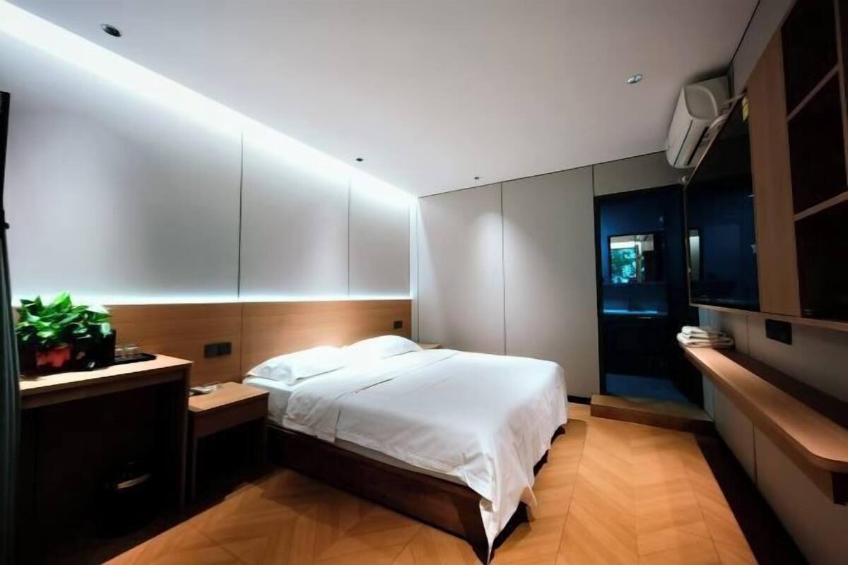 A modern hotel room with a bed, bedside table, and a small desk with a plant.