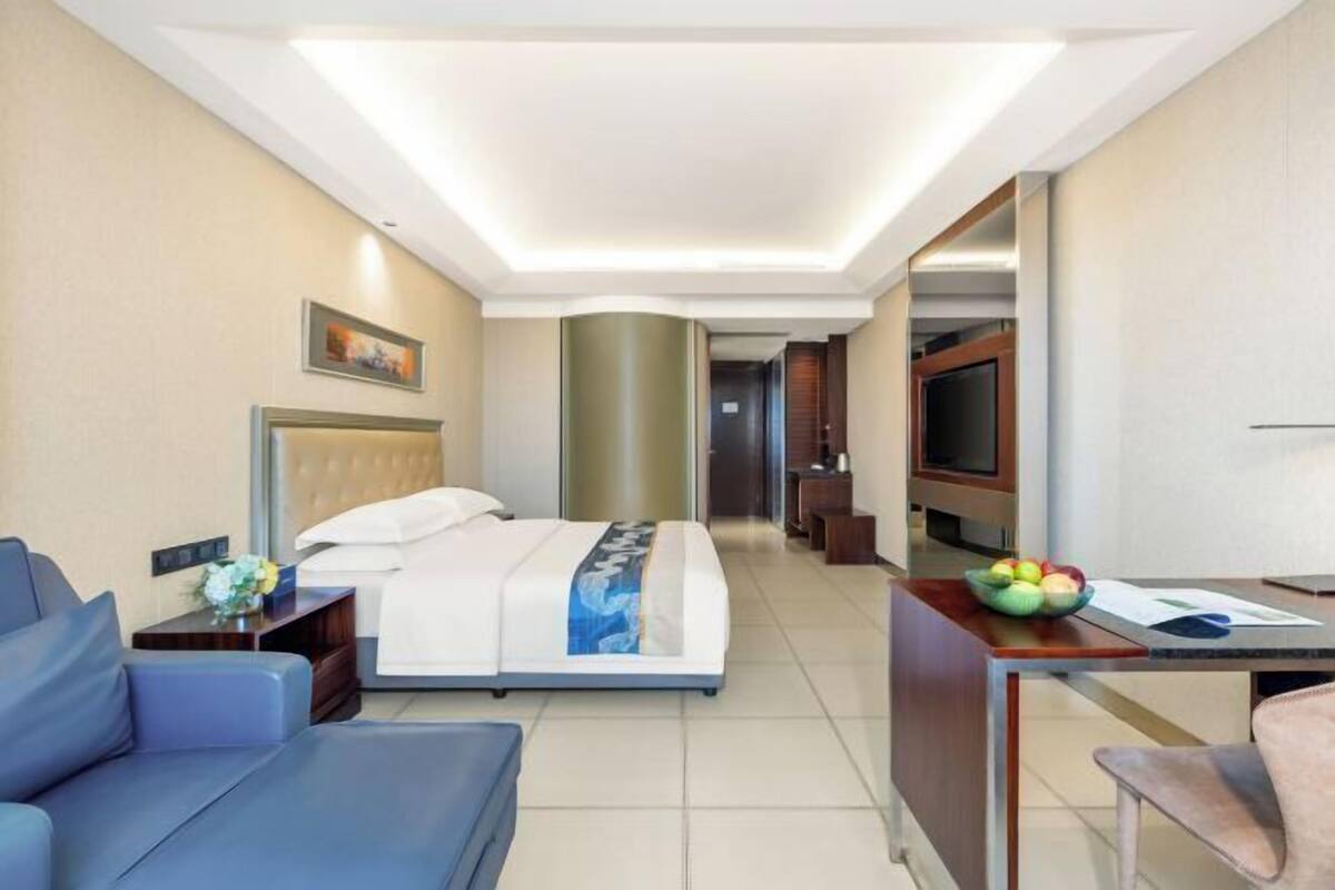 A hotel room with a bed, a desk, a chair, a TV, and a painting on the wall.