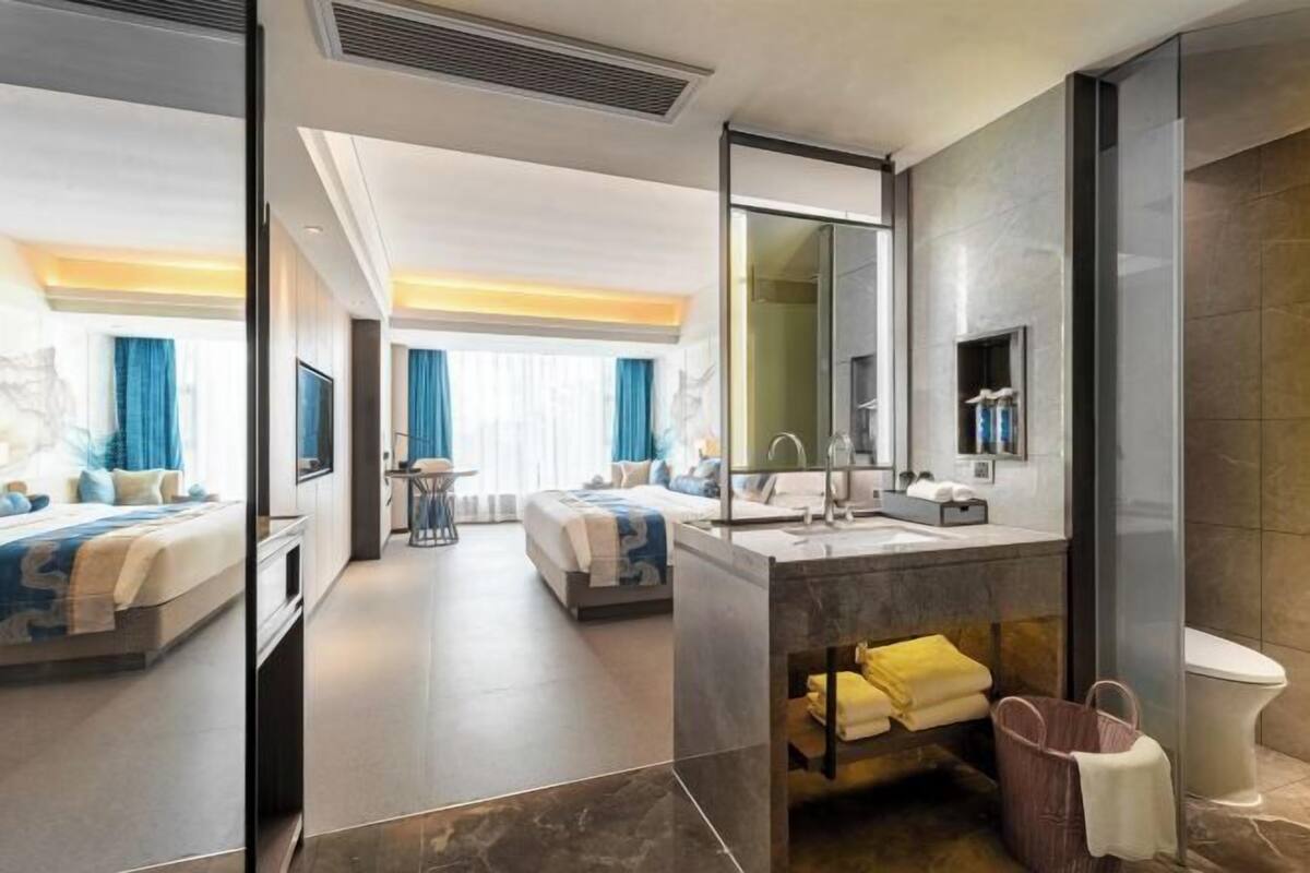 A modern hotel room with a large bed, a separate sitting area, a bathroom with a large mirror, and a flat-screen TV.