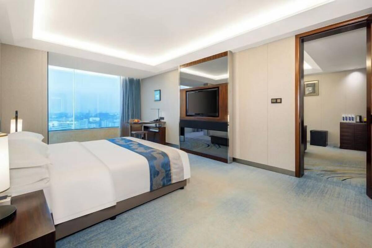 A hotel room with a large bed, a desk, a TV, and a view of the city.