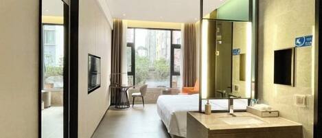 A hotel room with a large bed, a bathroom with a mirror, and a view of the outdoors.