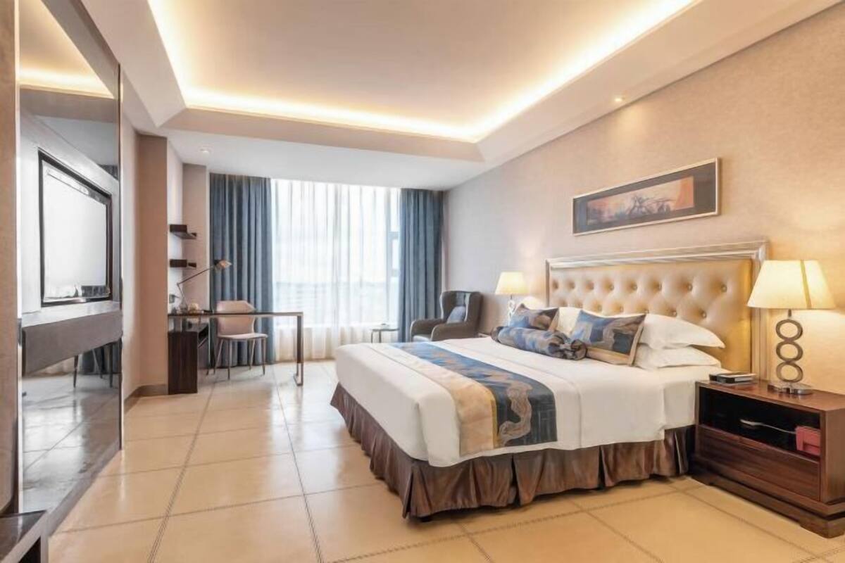 A hotel room with a large bed, a desk, a chair, and a TV.