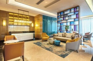 A modern hotel lobby with a marble reception desk, a sofa, and a seating area with chairs and a coffee table.