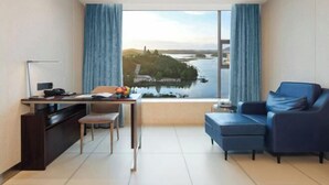 Un salon moderne avec vue sur un lac et une île au loin, un bureau avec une chaise et un canapé bleu.