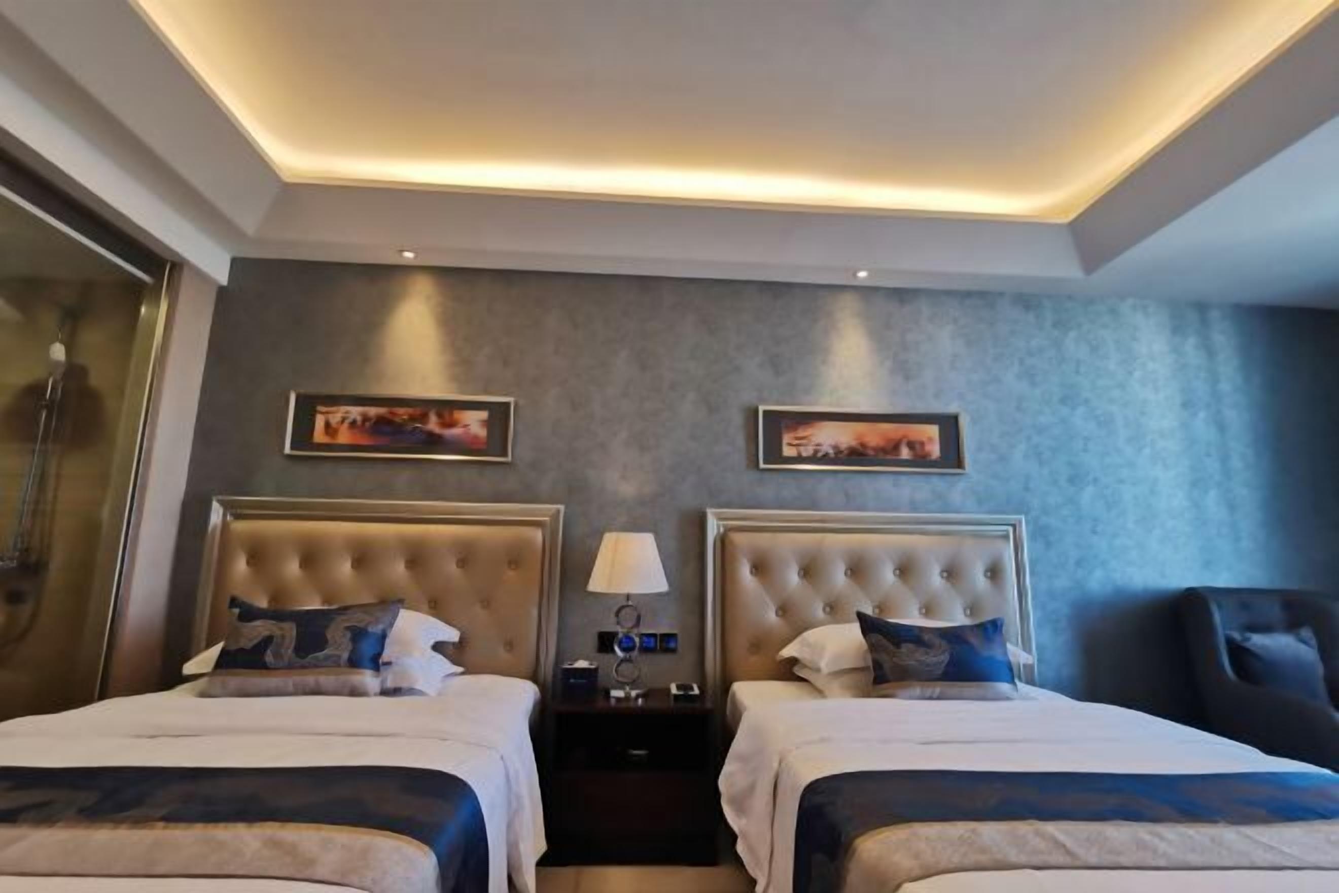 Hotellihuone, jossa on kaksi sänkyä, yöpöytä, tuoli ja taideteos seinällä.