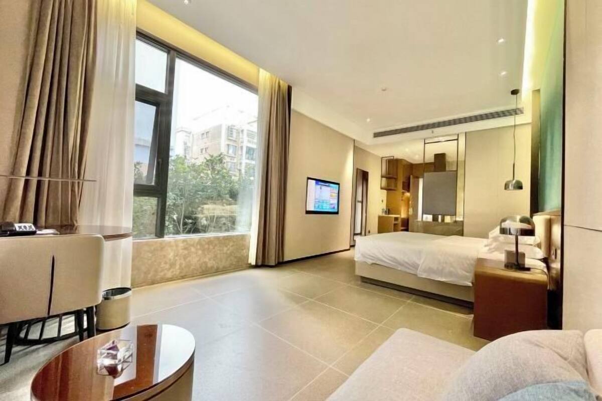 A modern hotel room with a bed, a desk, a TV, and a large window.