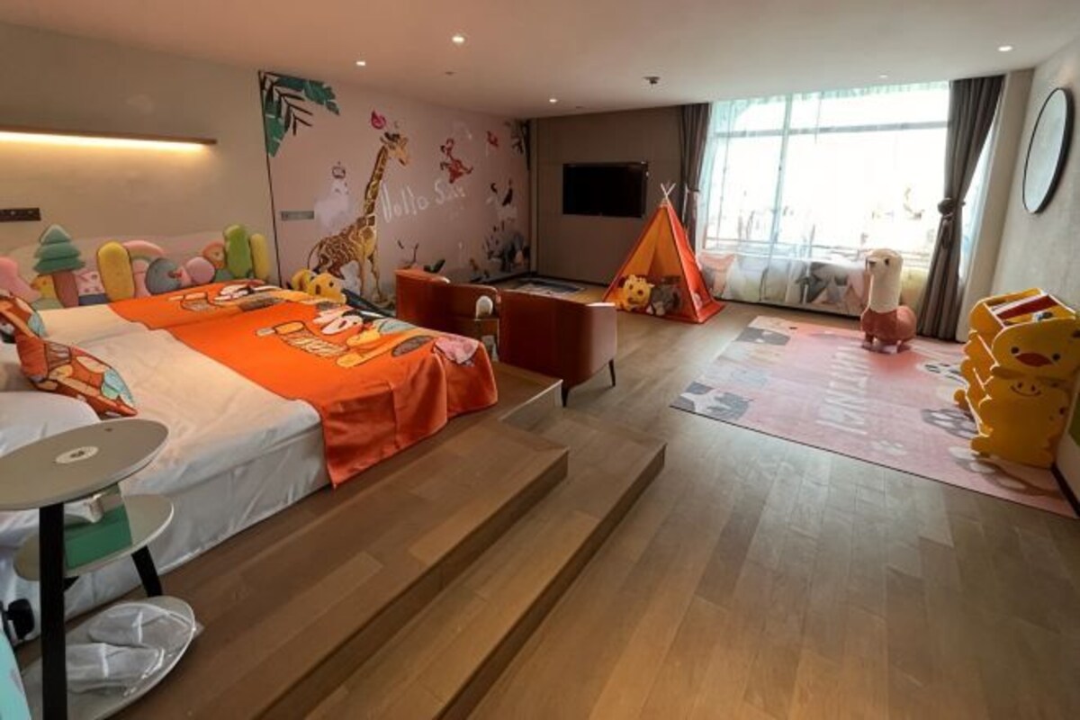 Habitación de hotel para niños, con cama, zona de juegos y un ventanal grande.