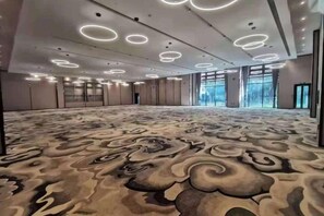 Un salón de conferencias amplio con alfombra estampada, luces empotradas en el techo y grandes ventanales.