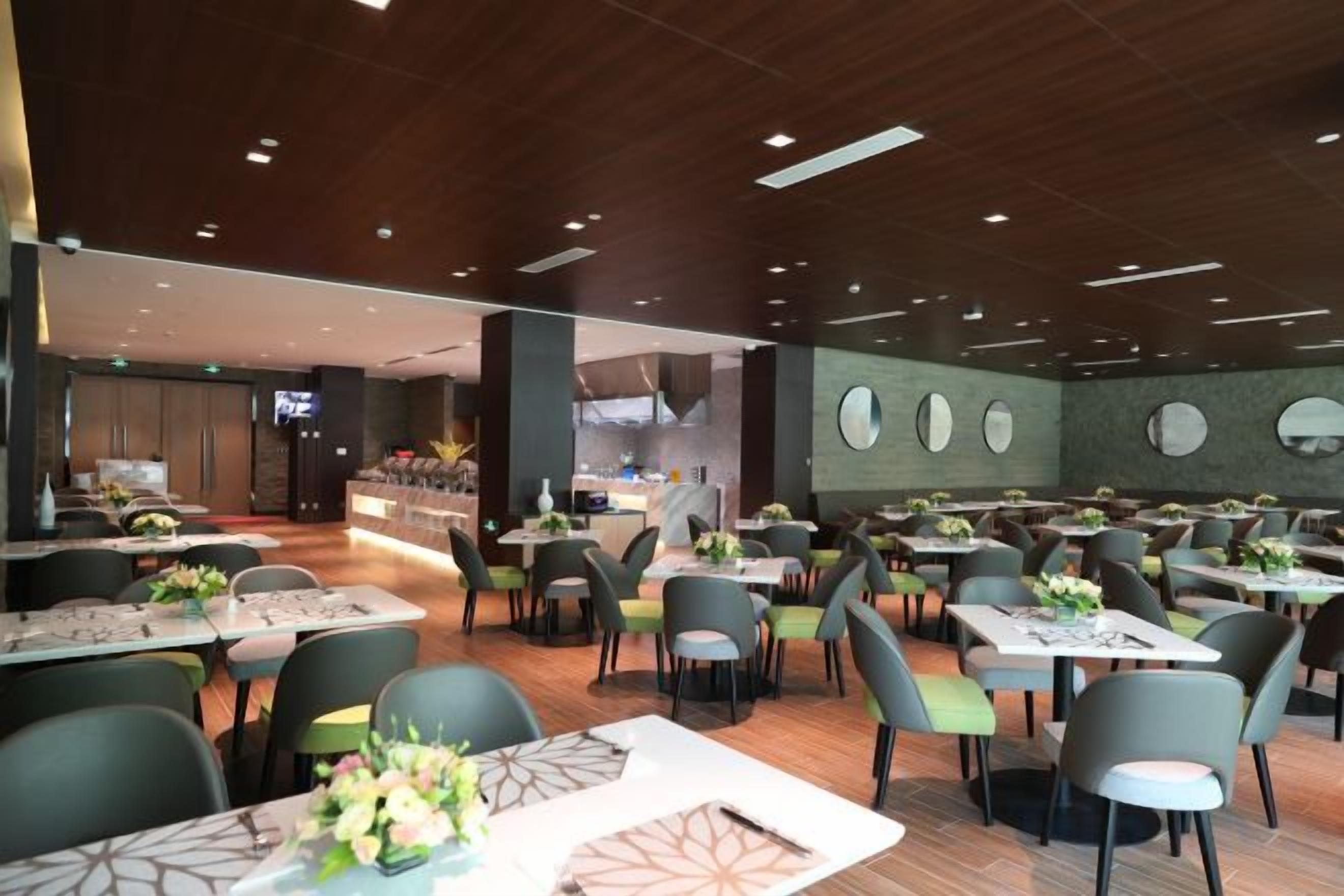 A modern restaurant with multiple dining tables and chairs, a bar area, and a kitchen in the background.